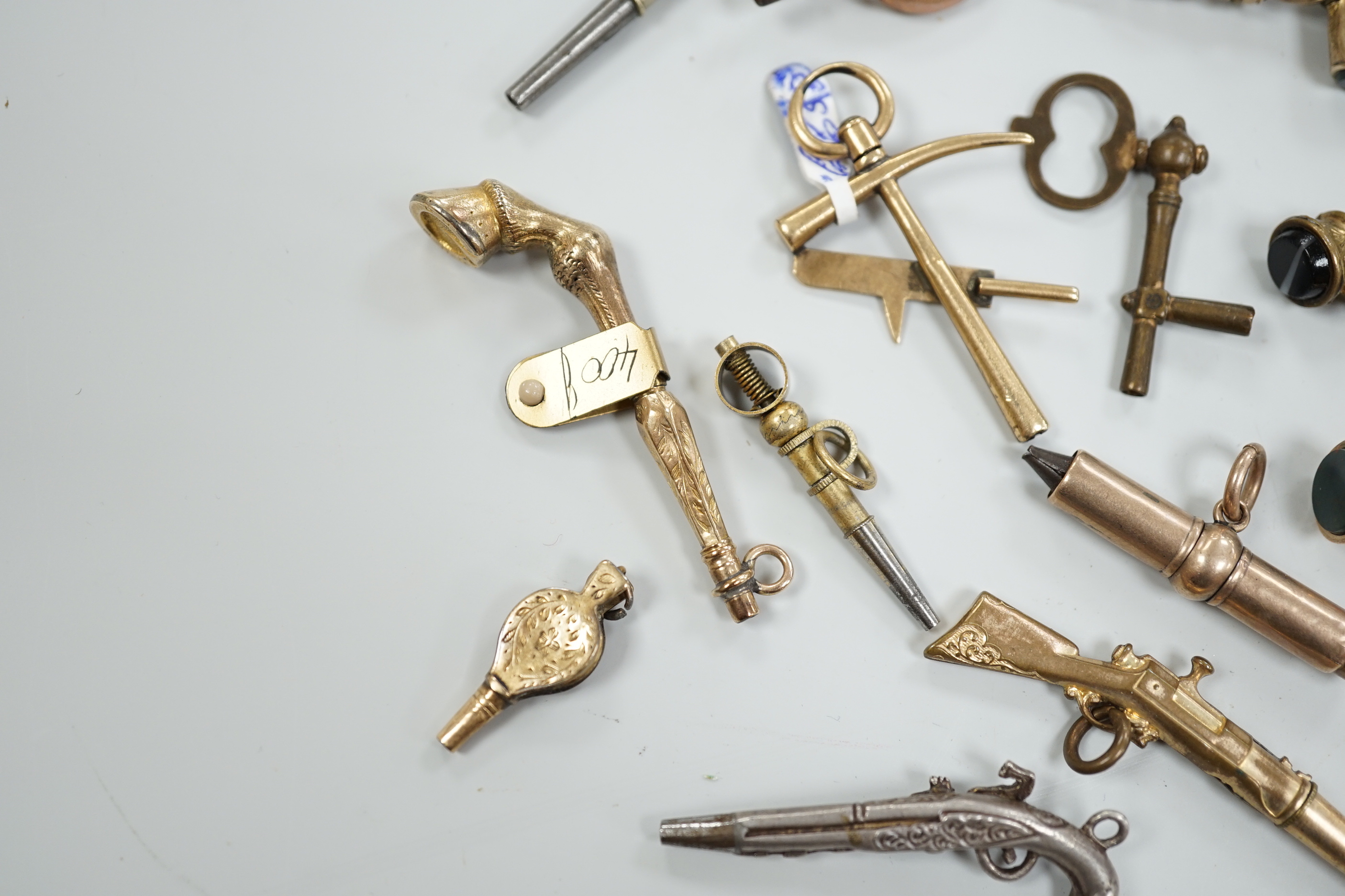 Eighteen assorted mainly 19th century base or yellow metal overlaid novelty watch keys, including coral and bloodstone set harp, pistol, rifle, cornucopia, bellows, horses hoof and trade insignia, largest 55mm.